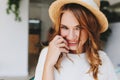 Close-up portrait of excited girl with elegant hairstyle smiling and shy touching face with hand. Indoor photo of fair Royalty Free Stock Photo