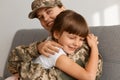 Close up portrait of extremely happy little dark haired girl hugging her mother soldier, woman wearing camouflage uniform and cap Royalty Free Stock Photo
