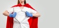 Close up portrait of a female doctor, wearing medical gloves and a red superhero Cape, tears her coat on her chest. Gray