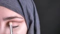 Close-up portrait of female hands doing eye make-up stumping with brush for beautiful muslim woman in hijab on black