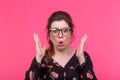 Close-up portrait of a frightened frustrated young pretty woman in glasses posing on a bright pink background. Concept