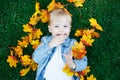 Close up portrait of funny cute smiling white Caucasian toddler child girl with blond hair lying on green grass with yellow leaves Royalty Free Stock Photo