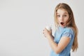 Close up portrait of funny good-looking little girl with light hair looking in camera with shocked expression, holding