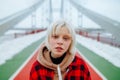 A close-up portrait of a girl in a blonde-haired shirt standing on a snow-covered bridge in winter and posing for the camera with Royalty Free Stock Photo