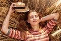 Close up portrait of girl resting in farm field, posing with closed eyes, holdiong her straw hat in hand, wearing striped shirt,