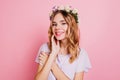 Close-up portrait of good-looking white woman in circlet of flowers smiling to camera. Indoor photo of enchanting blonde