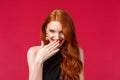 Close-up portrait of gorgeous silly and coquettish redhead girl acting, giggle and look from under forehead while