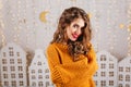 Close-up portrait of gray-eyed girl with curly hair posing in knitted sweater on light background with toy houses. Royalty Free Stock Photo