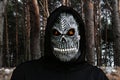 Close-up portrait of grim reaper. Man in death mask with fire flame in eyes on dark black woodland forest background Royalty Free Stock Photo