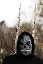 Close-up portrait of grim reaper. Man in death mask with fire flame in eyes on nature meadow with white flower Royalty Free Stock Photo