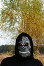 Close-up portrait of grim reaper. Man in death mask with fire flame in eyes on nature yellow birch tree background Royalty Free Stock Photo