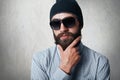 Close-up portrait of handsome bearded man wearing stylish black cap, checked shirt and sunglasses holding his hand on thick beard Royalty Free Stock Photo