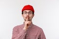 Close-up portrait of handsome bearded young man in glasses and red beanie, hiding secret, prepare special surprise, show Royalty Free Stock Photo