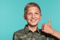 Close-up portrait of a blonde teenage boy in a green shirt with palm print posing against a blue studio background Royalty Free Stock Photo