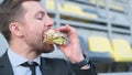 Close up portrait of a handsome hungry businessman appetizingly biting a cheeseburger.