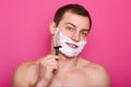 Close up portrait of handsome man with foam on face, shaving with razor in bathroom, looking smiling at camera, posing with bared Royalty Free Stock Photo