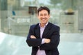 Handsome mature man in business suit posing with arms crossed outdoors and smiling