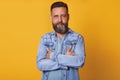 Close up portrait of handsome middle aged Caucasian man with beard, posing isolated on yellow background, wears denim jacket and Royalty Free Stock Photo