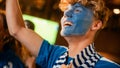 Close Up Portrait of a Handsome Young Soccer Fan with Painted Blue and White Face Standing in a Royalty Free Stock Photo