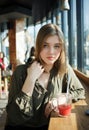 Close up portrait of happy beautiful teen student girl with a glass mug straw fruit tea at street cafe sitting near big window Royalty Free Stock Photo