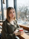 Close up portrait of happy beautiful teen student girl with a glass mug straw fruit tea at street cafe sitting near big window Royalty Free Stock Photo