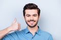 Close up portrait of the happy brunet`s model face in jeans shirt on lifgt background showing thumb up sign