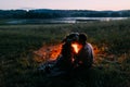 Close-up portrait of the happy couple sitting back embracing by fire at night. Girl in wreath