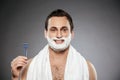 Close up portrait of happy man with shaving foam on his face holding razor, isolated over gray background Royalty Free Stock Photo