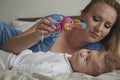 Close-up portrait of happy mother with her baby on bed in bedroom. Young blonde mom playing with her son. Baby looking at the toy Royalty Free Stock Photo