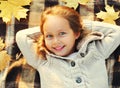 Close up portrait of happy smiling little girl child lying on a plaid with yellow maple leaves in autumn day Royalty Free Stock Photo