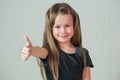 Close-up portrait of happy smiling little girl with long hair showing super sign with her thumbs up Royalty Free Stock Photo