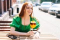 Close-up portrait of happy smiling young woman drinking cocktail through straw sitting at table in outdoor cafe in sunny Royalty Free Stock Photo