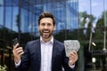 Close-up portrait of a happy, successful and rich young businessman standing outside an office building, holding a phone Royalty Free Stock Photo