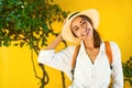 Close-up portrait happy woman tourist in straw hat, white shirt smiling and looking to camera, bright yellow wall on Royalty Free Stock Photo