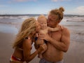 Close up portrait of happy young Caucasian family. Father holding baby boy. Parents kissing their son. Family time on the beach. Royalty Free Stock Photo