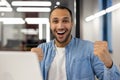 Close-up portrait of a happy young hispanic man sitting in a modern office in front of a laptop and looking at the Royalty Free Stock Photo