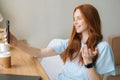 Close-up portrait of happy young woman making selfie on mobile phone sitting at table with laptop by window in cafe. Royalty Free Stock Photo