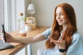 Close-up portrait of happy young woman making selfie on mobile phone sitting at table with laptop by window in cafe. Royalty Free Stock Photo