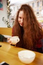 Close-up portrait of happy young woman making selfie on mobile phone sitting at table with laptop by window in cafe Royalty Free Stock Photo