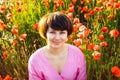 Close up portrait of happy young woman in a pink dress relaxing in red poppies flowers meadow in sunset light. A simple pleasure