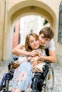 Close-up portrait of happy young woman in wheelchair and her husband, looking at camera and smiling, walking outdoors in Royalty Free Stock Photo