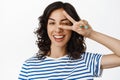 Close up portrait of happy young woman, winking and showing peace v-sign gesture, kawaii sign, smiling white teeth