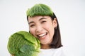 Close up portrait of healthy smiling asian woman, showing cabbage, green letture, with leaf on head, isolated on white Royalty Free Stock Photo