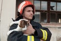 Close-up portrait of heroic fireman in protective suit and red helmet holds saved cat in his arms. Firefighter in fire