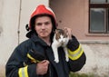 Close-up portrait of heroic fireman in protective suit and red helmet holds saved cat in his arms. Firefighter in fire