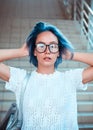 Close-up portrait of a hipster girl wearing glasses with blue hair. Atypical beauty.