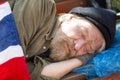 Close up portrait of homeless man sleeping on bench in city park.