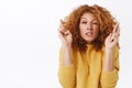 Close-up portrait hopeful, worried cute redhead curly woman in yellow sweater, stooping and grimacing with closed eyes