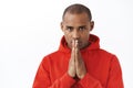 Close-up portrait of hopeful young determined african american man in red hoodie, praying, awaiting important news