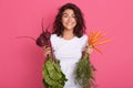 Close up portrait of hungry pleasant sweet brunette standing isolated over pink background, holding raw vegetables, having beet Royalty Free Stock Photo